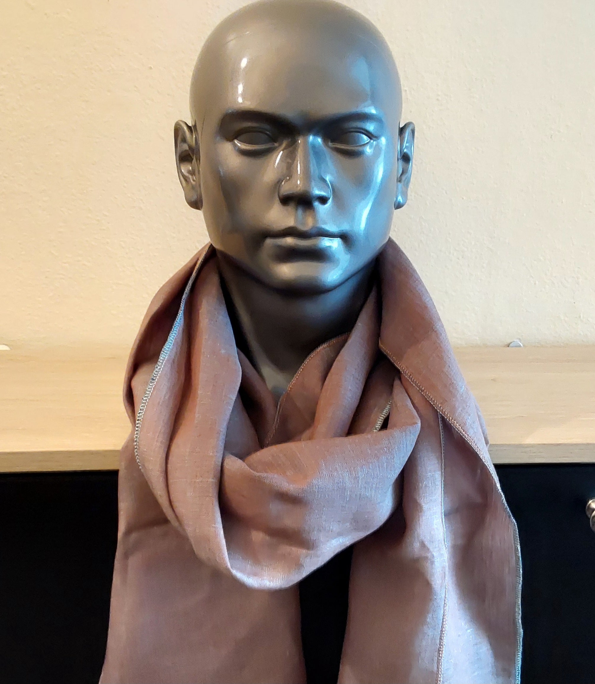 Mannequin head wearing a pink scarf against a neutral background