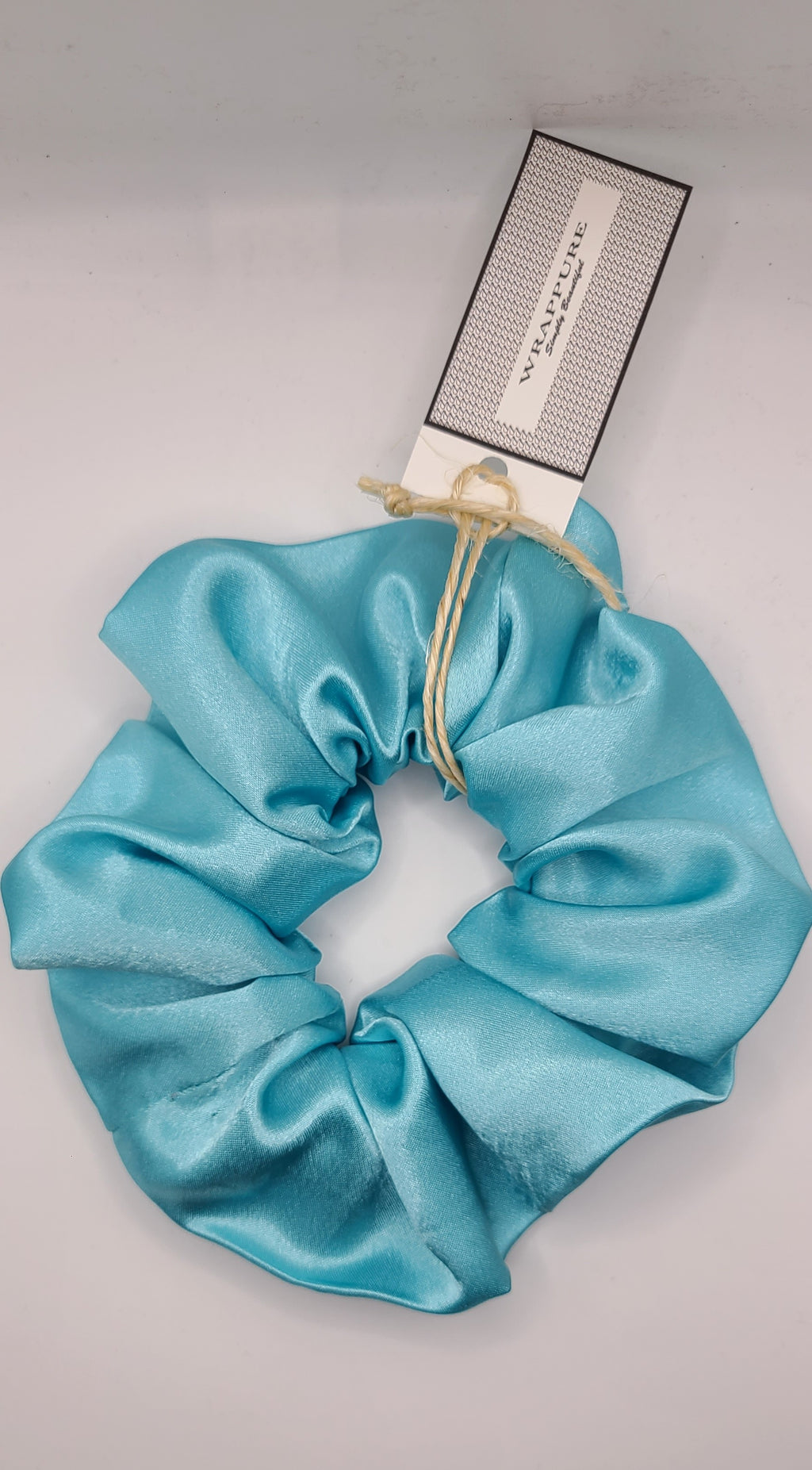 Turquoise scrunchie with a brand tag on a light gray background