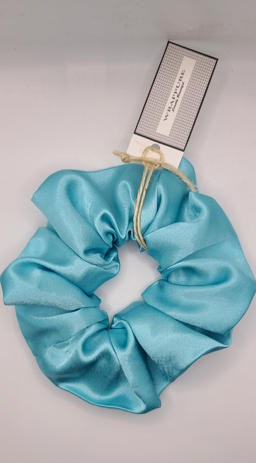 Turquoise scrunchie with a brand tag on a light gray background