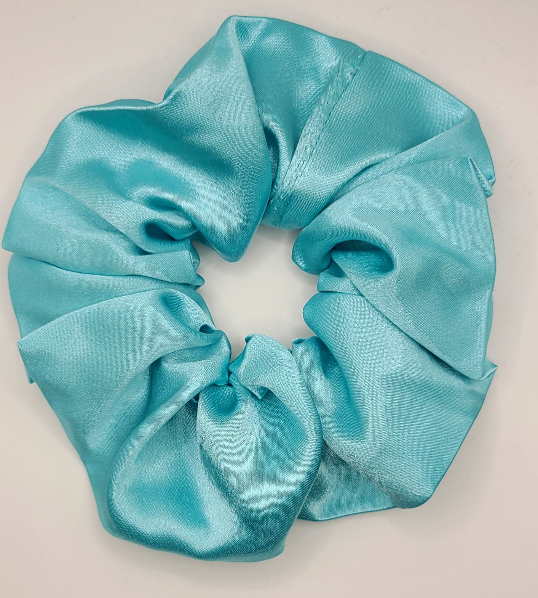 Turquoise satin scrunchie on a light gray background