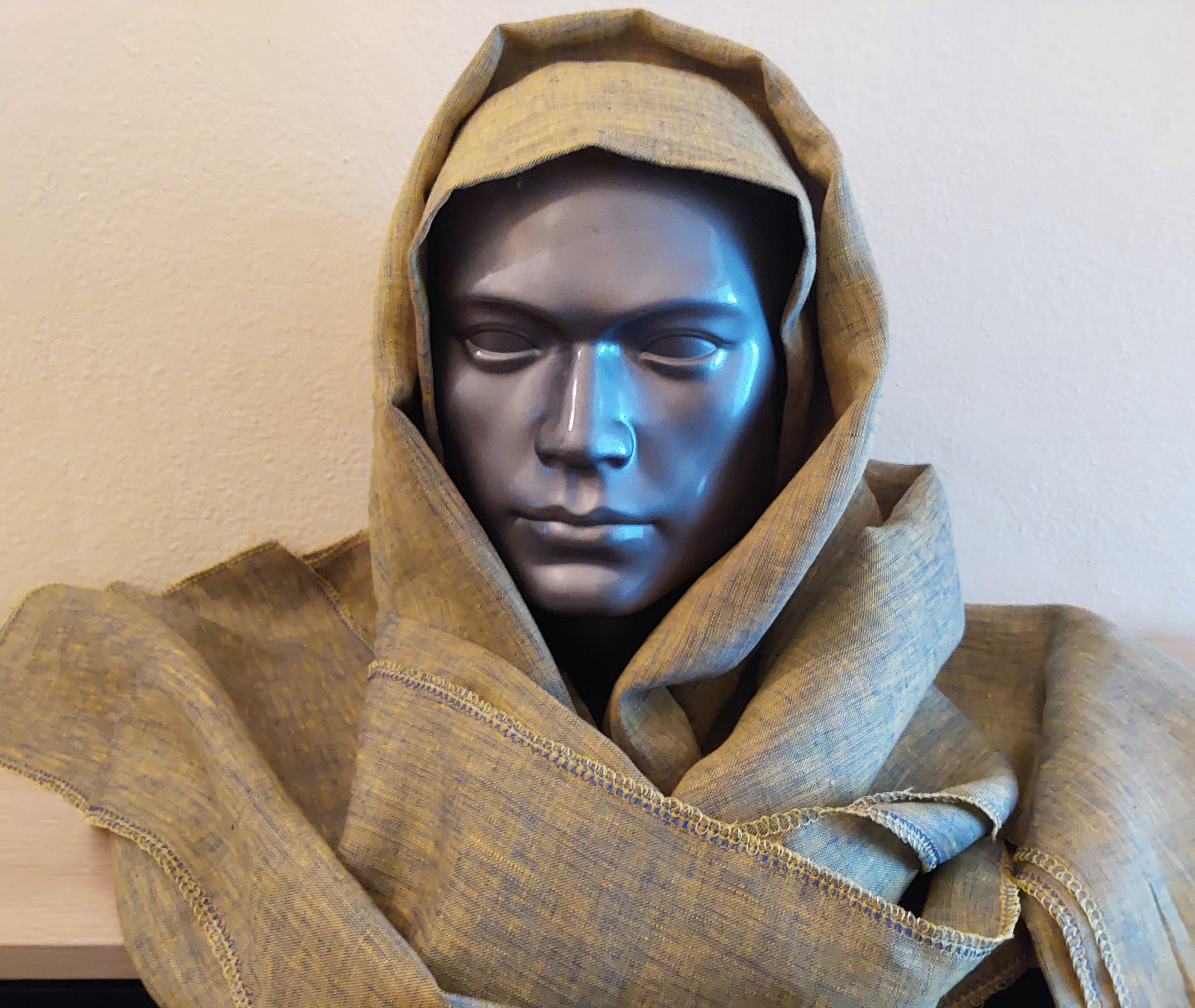 Mannequin head wearing a greenish brown hooded garment against a plain background