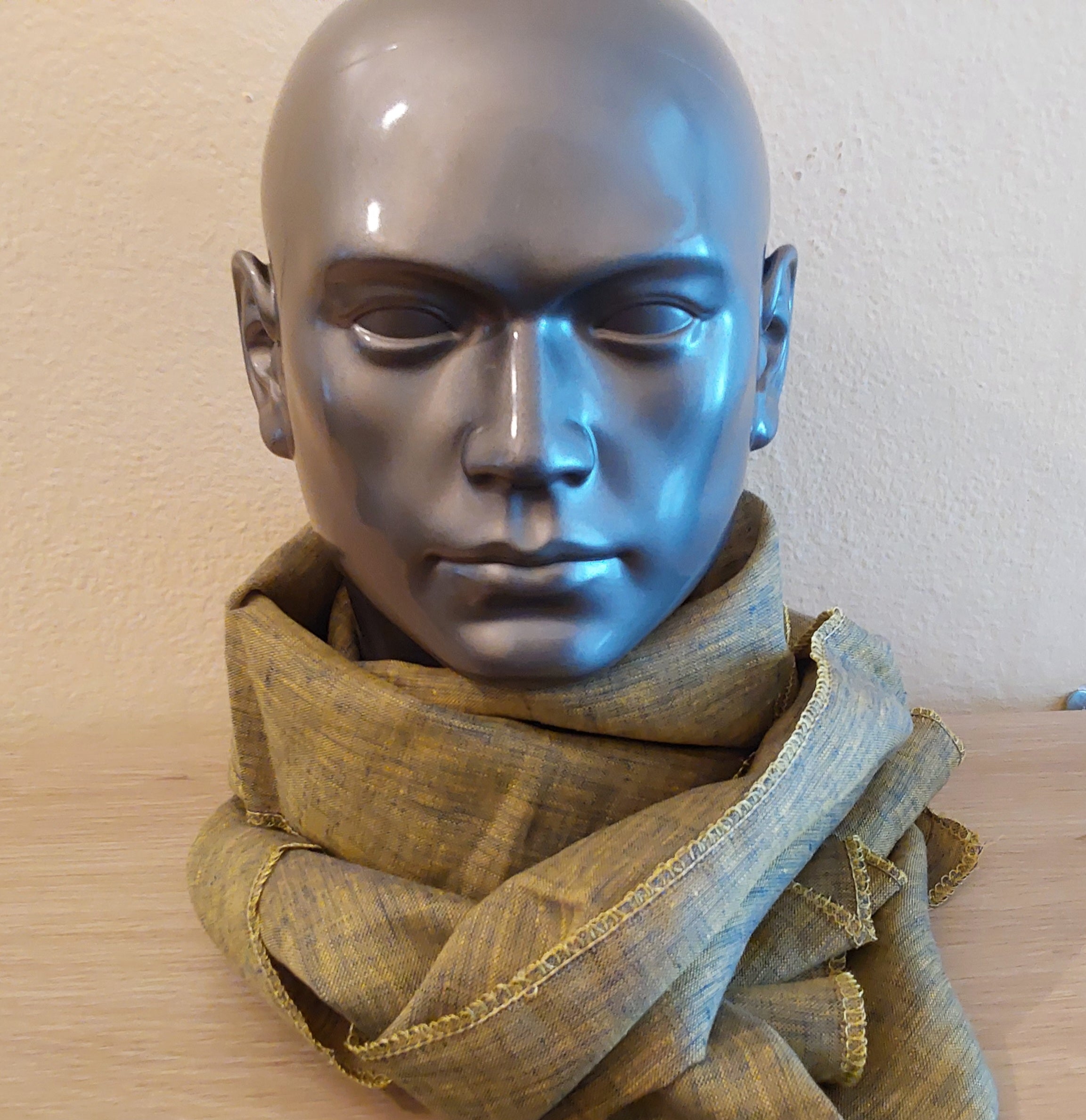 Mannequin head wearing a green and yellow scarf against a plain background