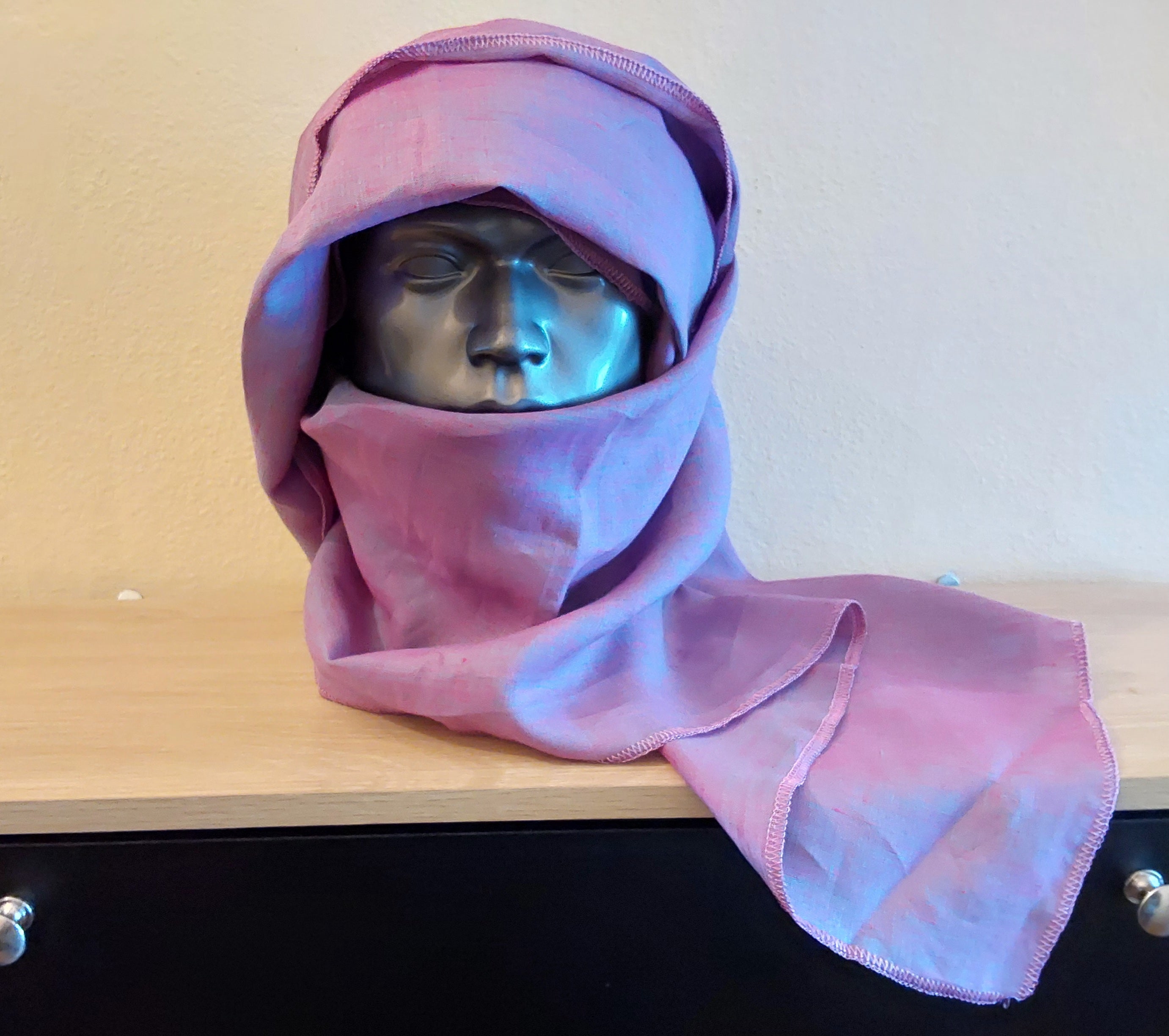 Mannequin head wearing a purple hooded garment on a wooden surface.