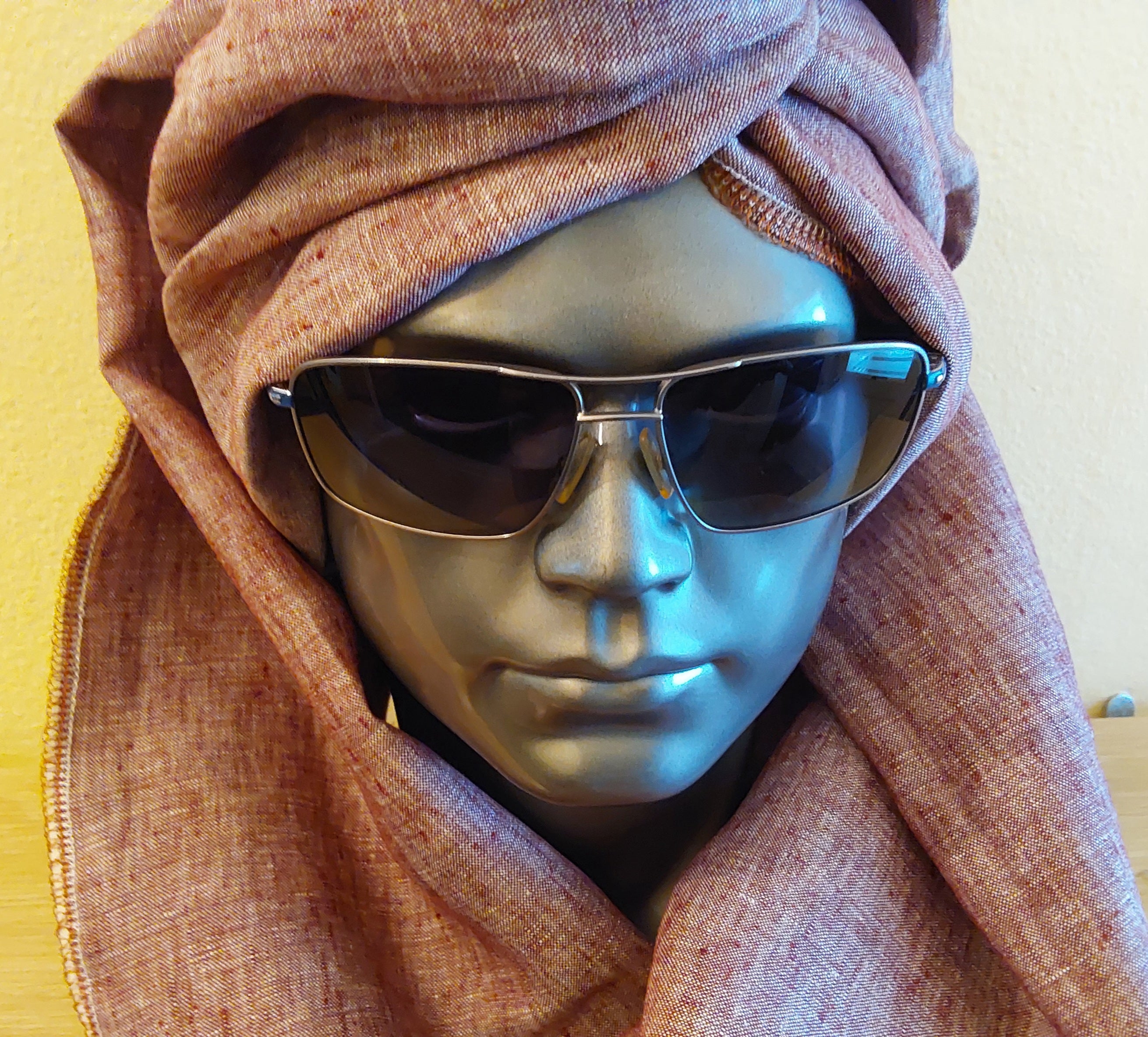 Mannequin head wearing a reddish brown hijab and dark sunglasses on a yellow background