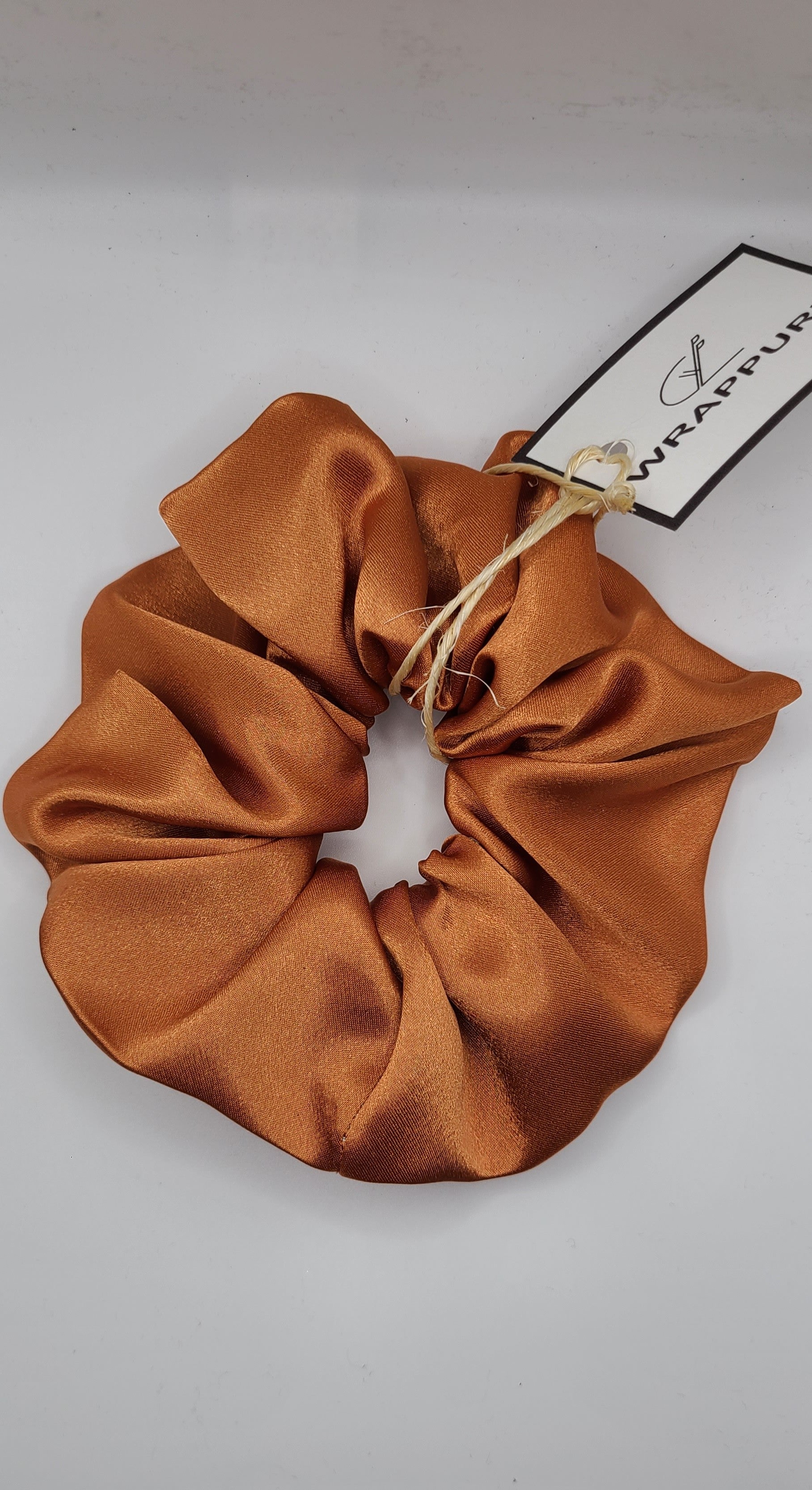 golden Brown satin scrunchie with a tag on a light gray background