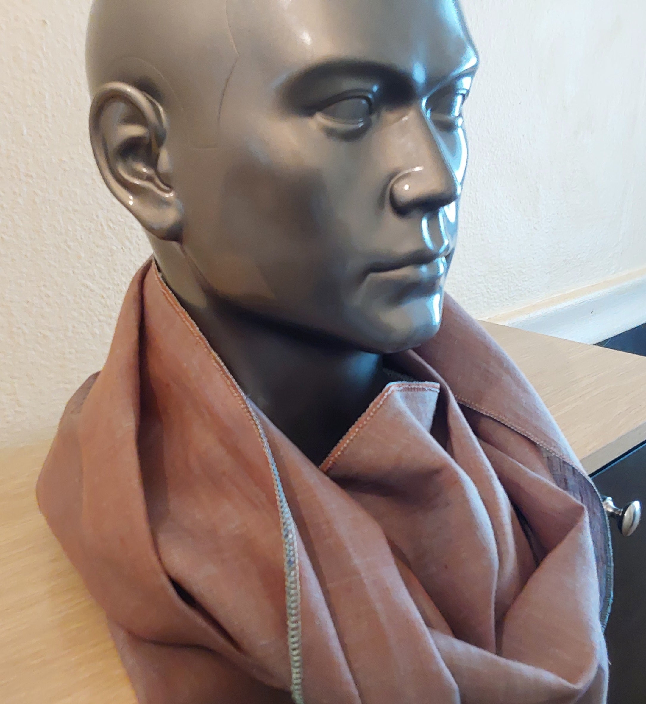 Mannequin head with a brown scarf draped over it on a light-colored surface.