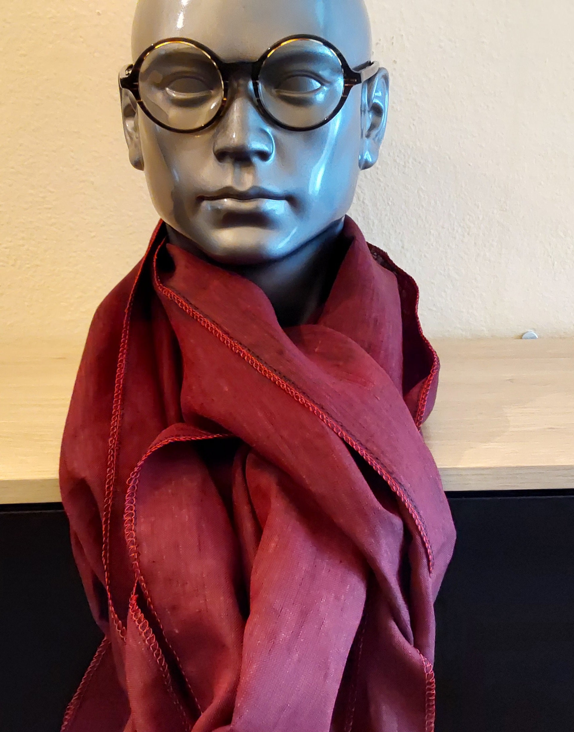 Mannequin head wearing a red scarf and black glasses against a neutral background