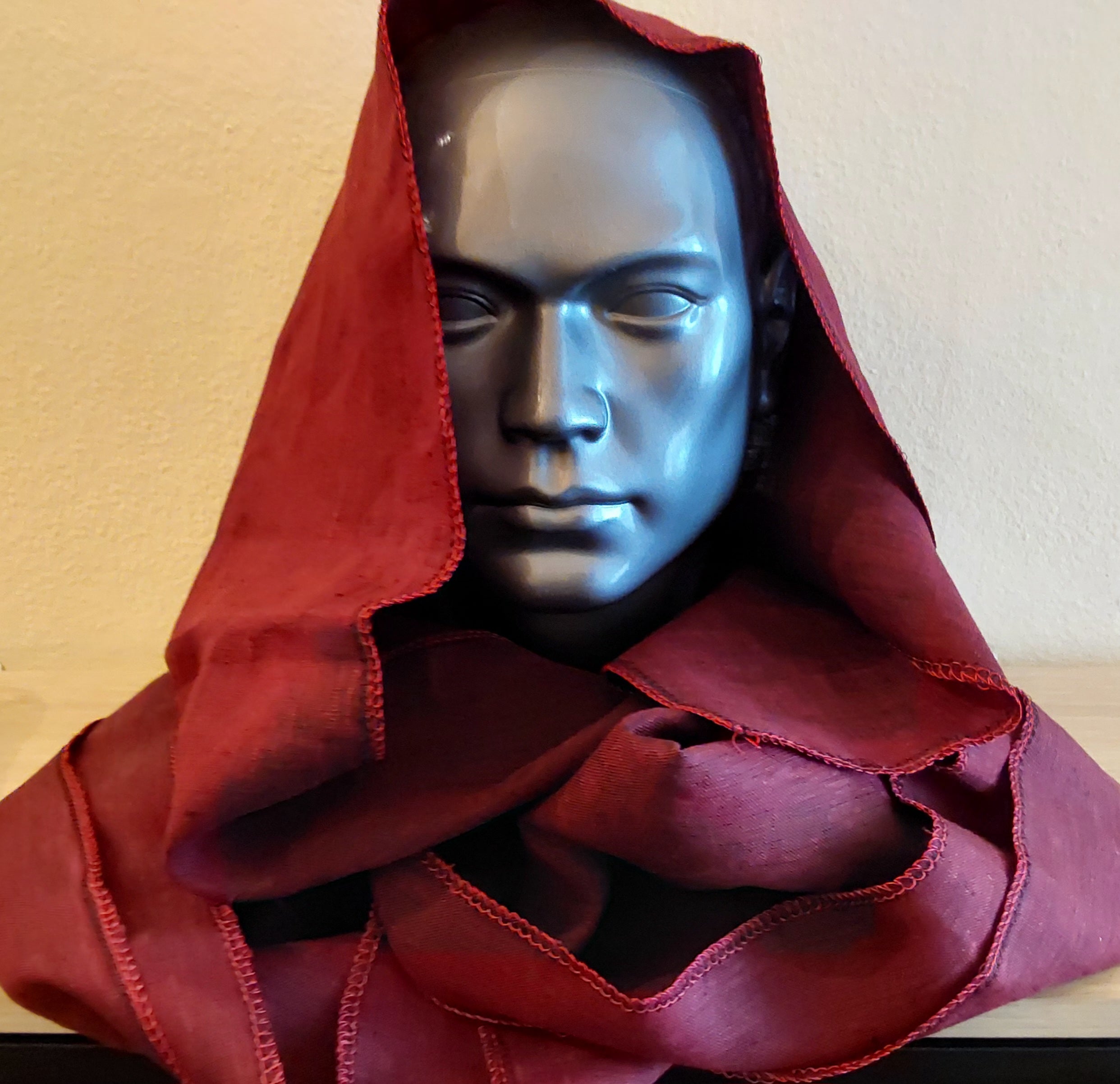Bust wearing a red hood against a plain background
