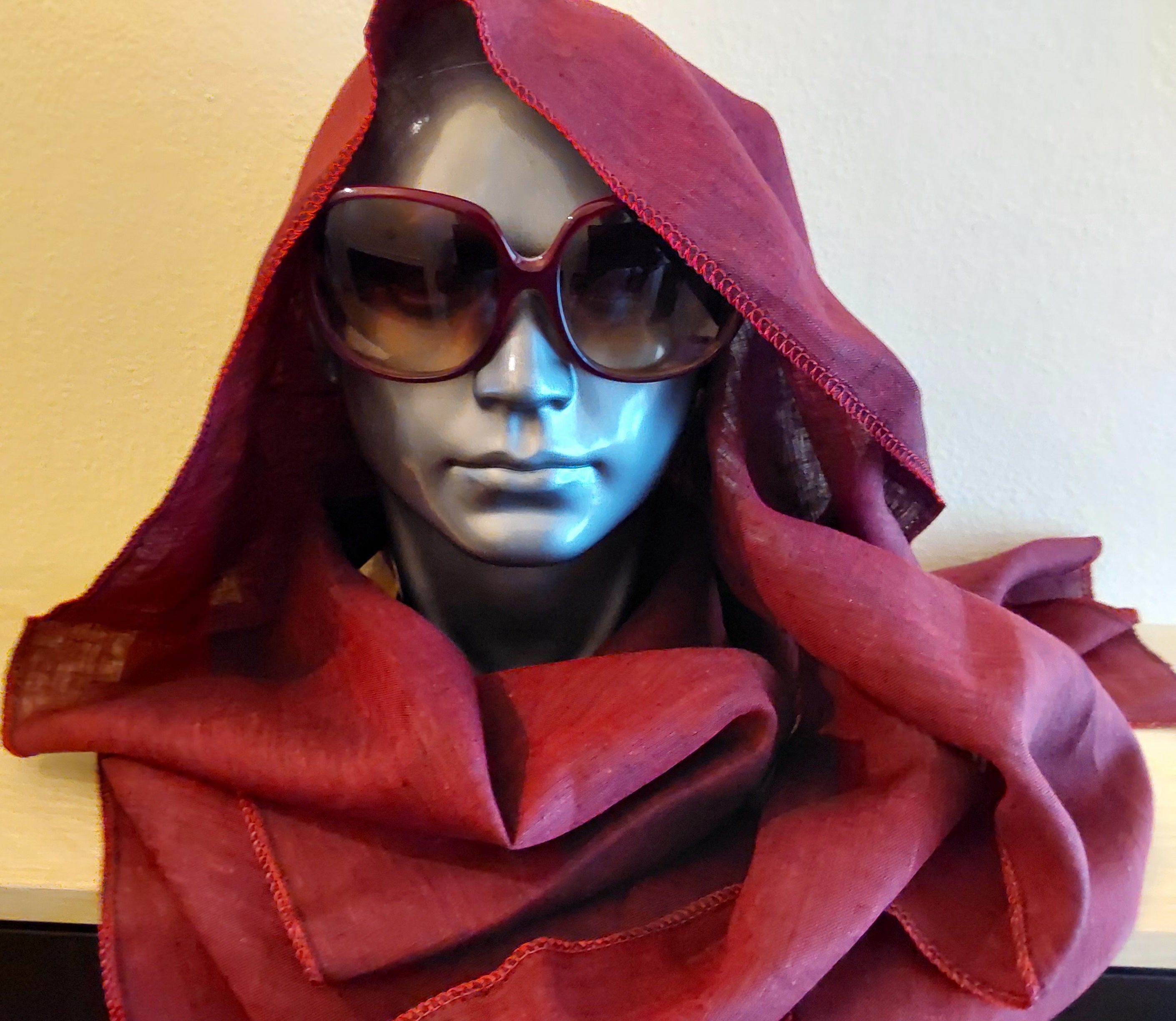 Mannequin head wearing a red scarf and sunglasses against a plain background