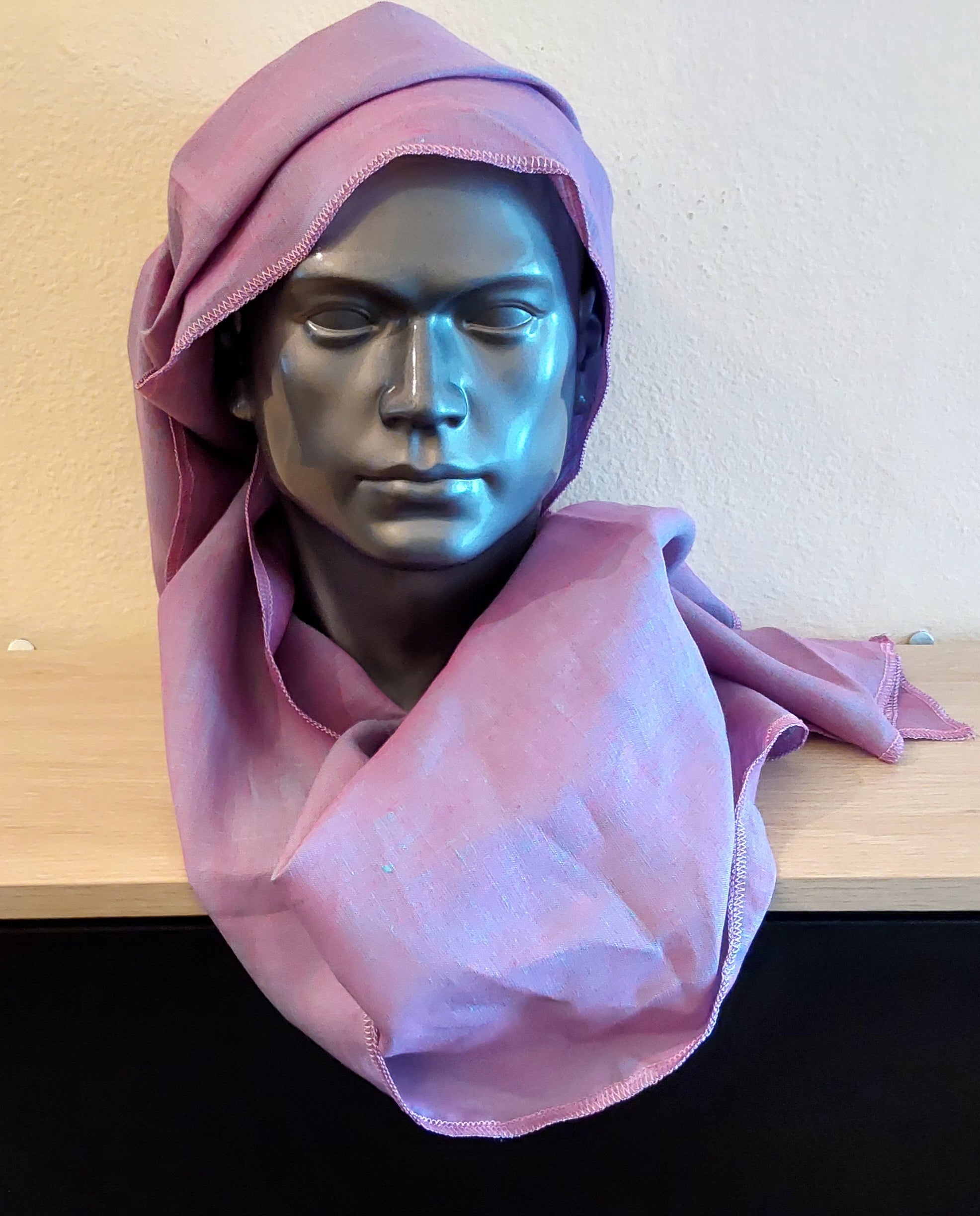 Mannequin head with a purple hijab draped over it on a wooden surface.