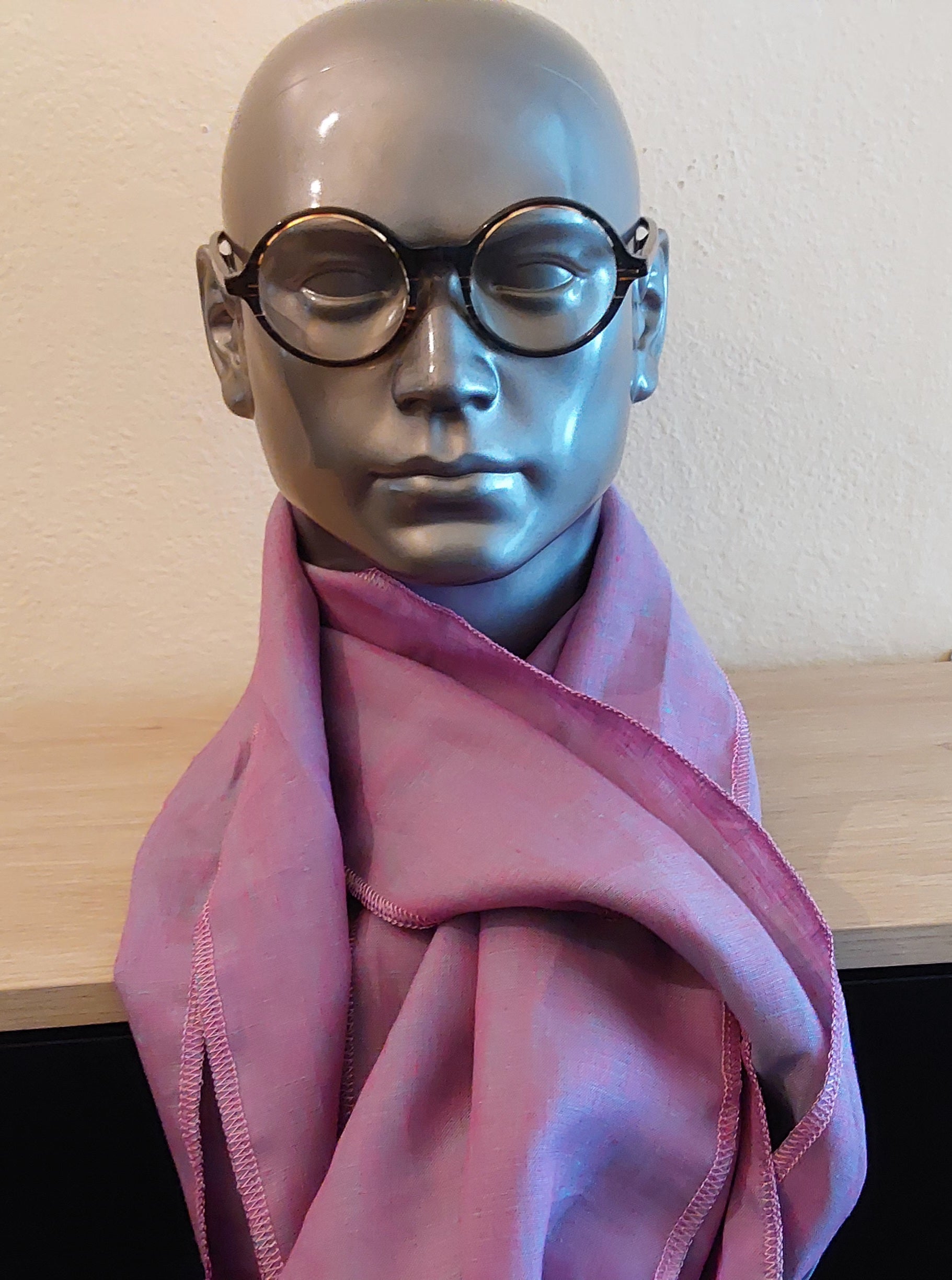 Mannequin head with purple scarf and glasses on a wooden surface