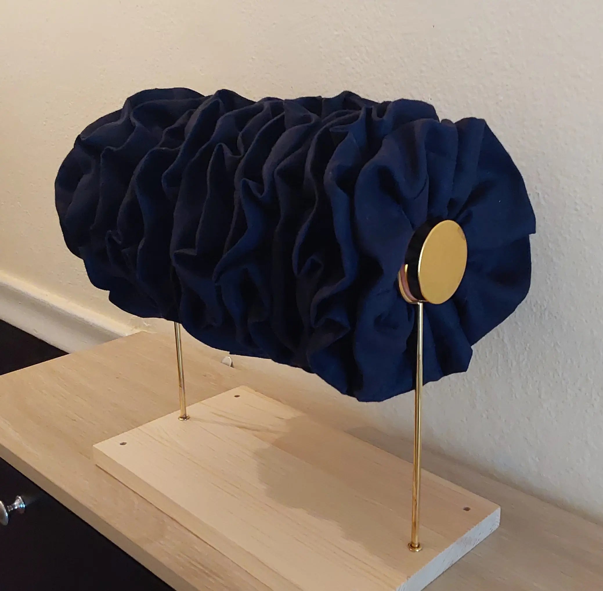 Navy blue headband on a wooden stand with a gold circular component against a white wall.