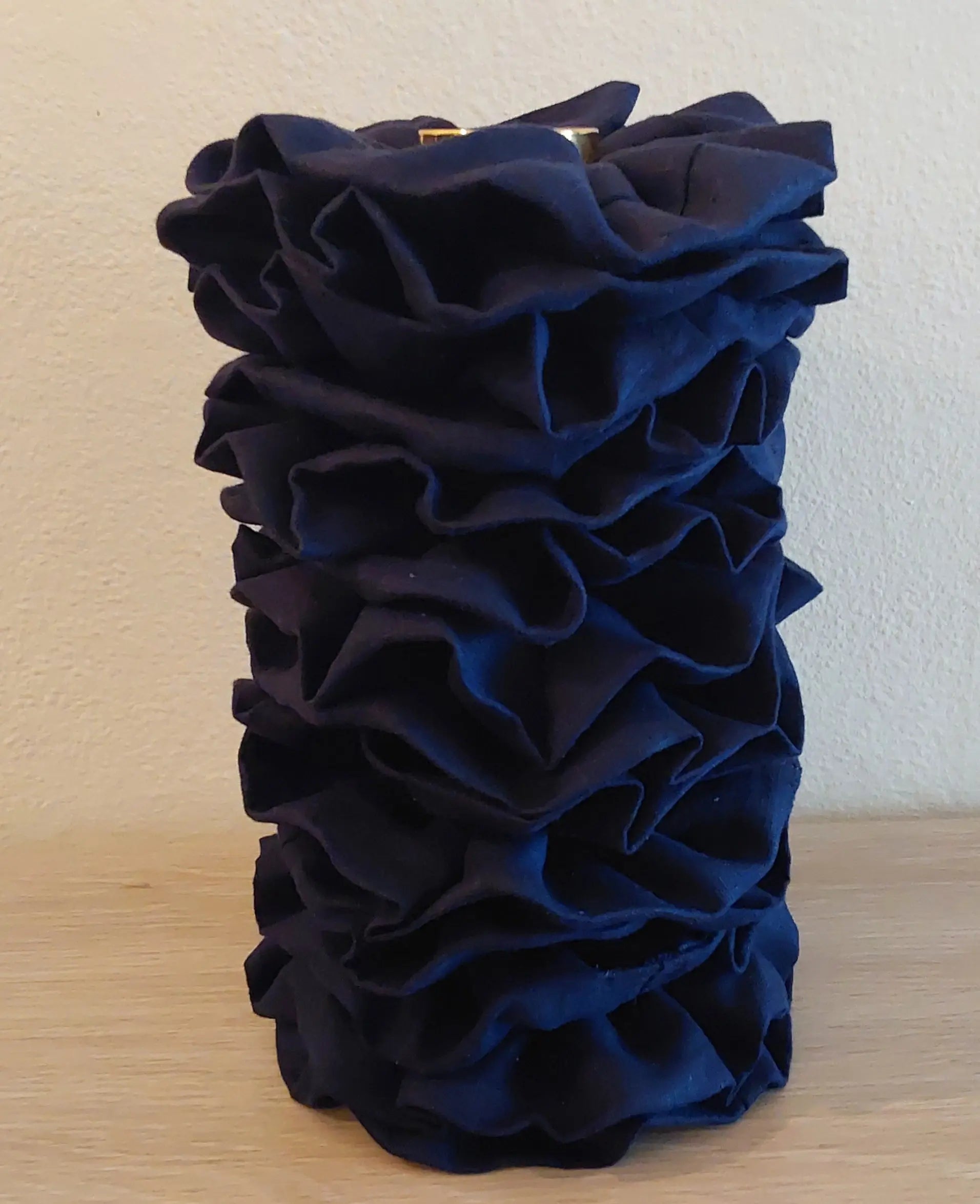 Navy blue ruffled vase on a wooden surface with a plain background