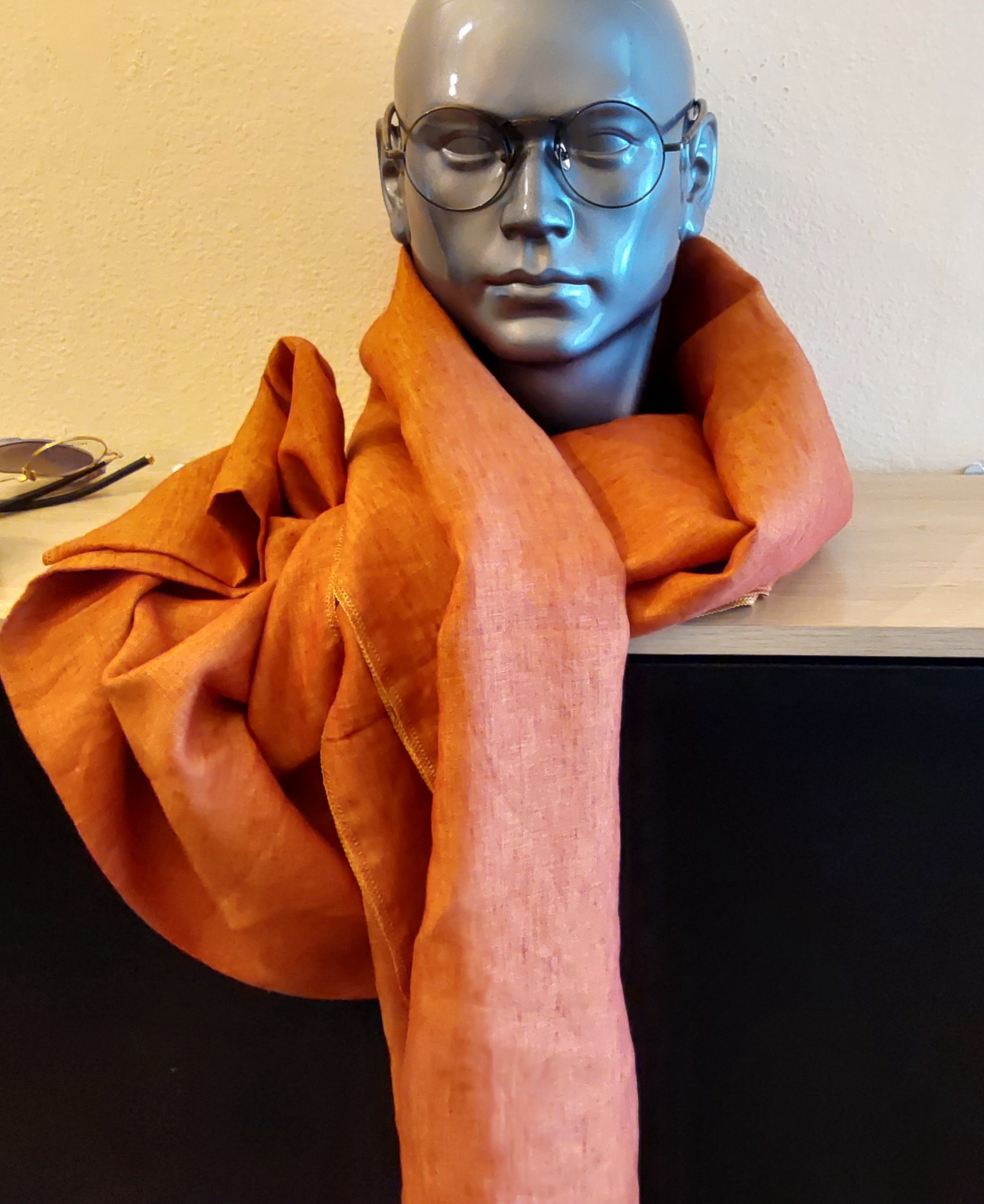 Mannequin wearing a  orange colored scarf with a neutral background