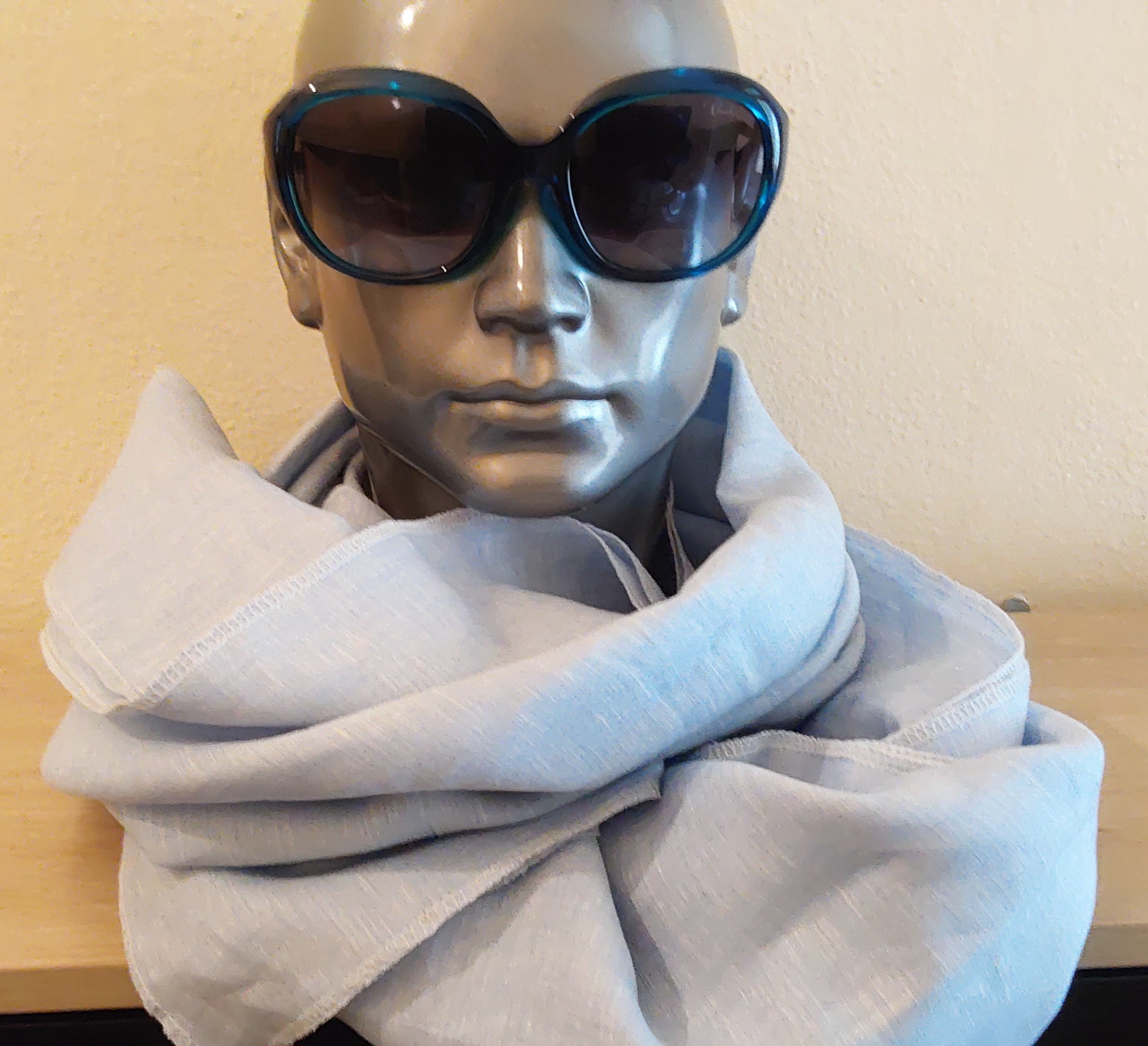 Mannequin wearing a light blue scarf and dark sunglasses against a plain background